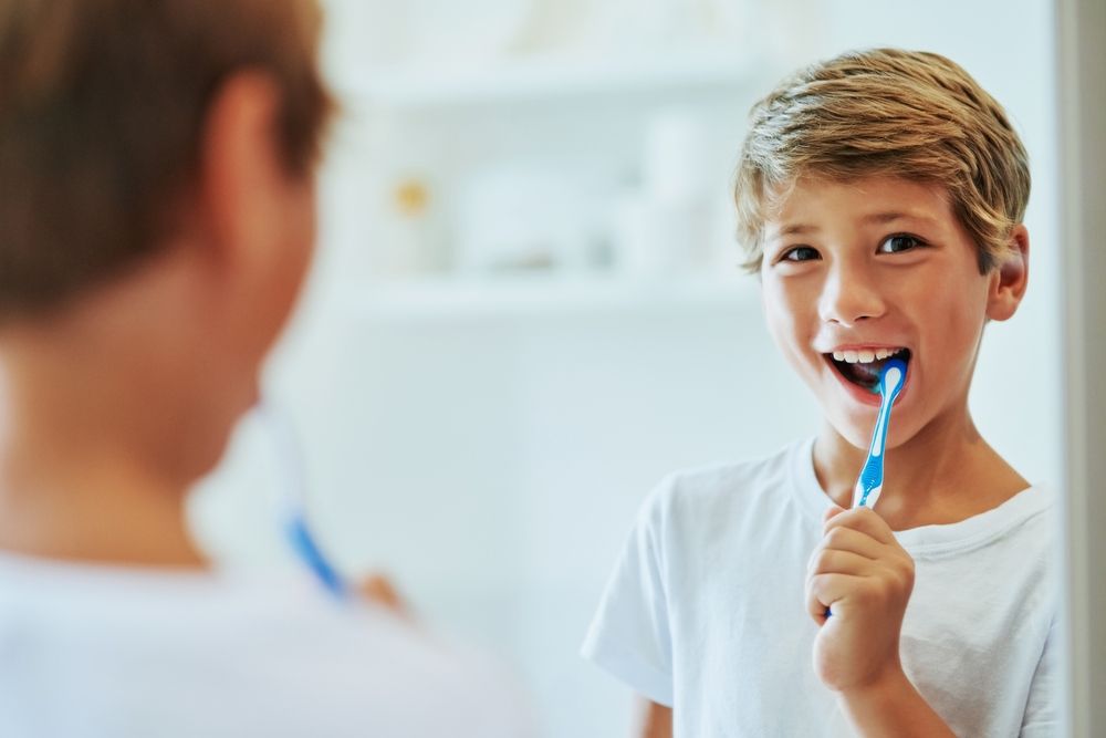 young child smiling and brushing their teeth in the mirror