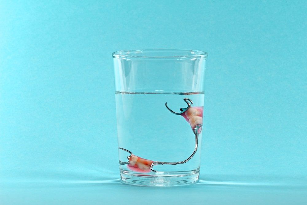 partial denture in glass of water on teal background