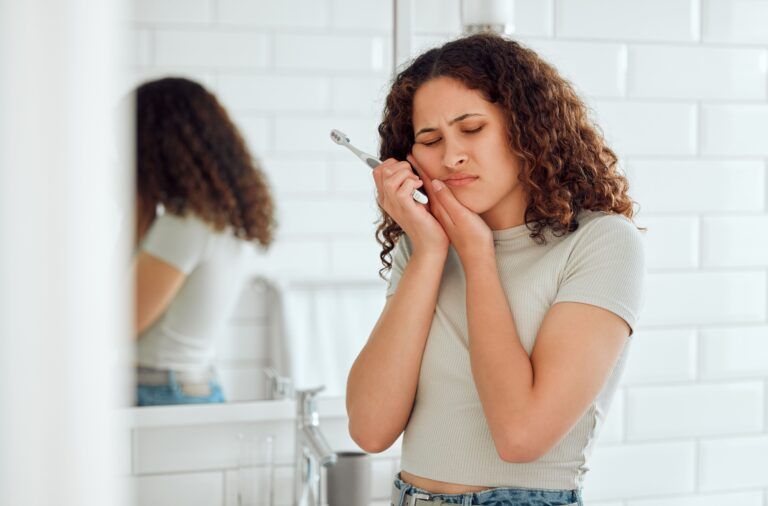woman holding toothbrush and her cheek in pain