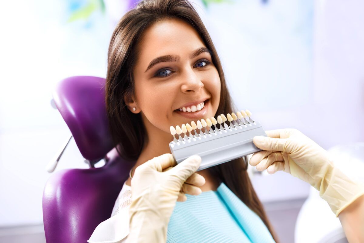 woman sitting in dental chair planning teeth whitening procedure with shade guide